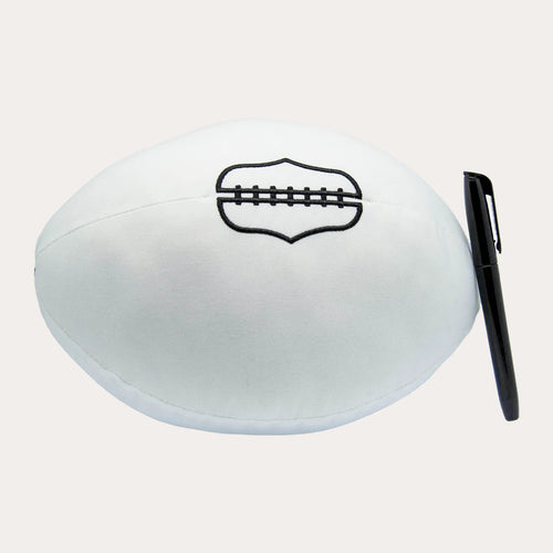 Oval white plush signature football shot side on against white, with soft signable fabric panels and a black embroidered lacing panel outline on the top face. A capped black permanent marker lies upright beside it for scale.