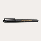 Capped black gloss permanent marker shown side on against white, printed "Congratulations" in gold italic script along the barrel, with a moulded black pocket clip and rounded ends.