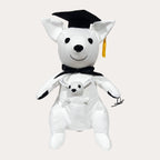 White plush kangaroo shot straight on with a joey sitting in its front pouch, wearing a black felt mortarboard with a yellow tassel and a black satin ribbon tied in a bow at the neck. Glossy black eyes and nose, plain white plush ears with no dark tips and black-tipped paws against a cream backdrop.